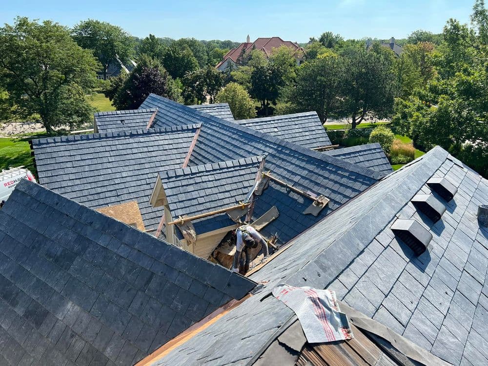 Rooftop view of a slate roof installation on residential houses surrounded by trees.